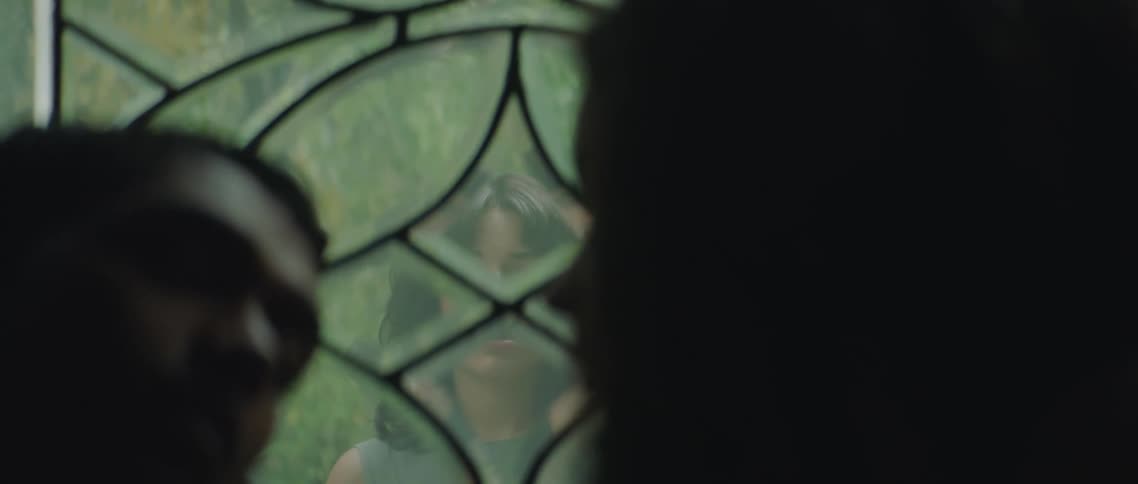 A woman looks though a window at a couple inside as they look into each others eyes romantically
