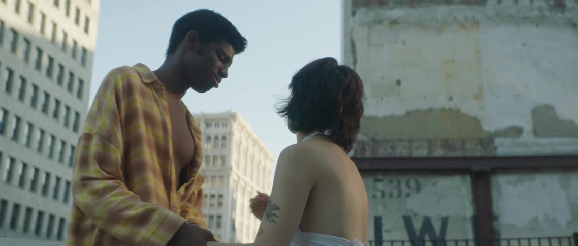 A man and woman face one another while holding hands outdoors in a metropolis during the day