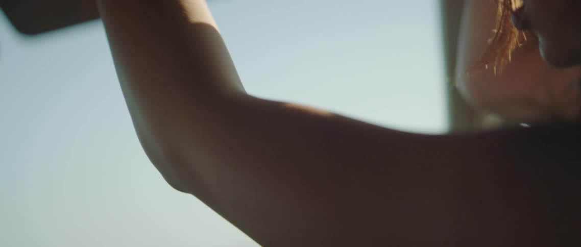 A teenage girl sits in a vehicle and raises her arms up