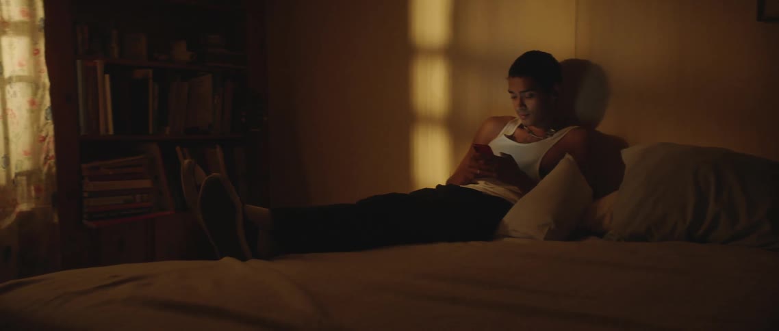 Man reclines on bed against pillows using mobile phone