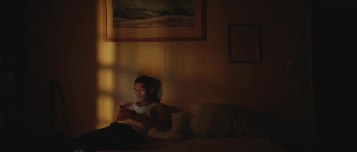 A teenage boy sits on a bed and uses a cell phone