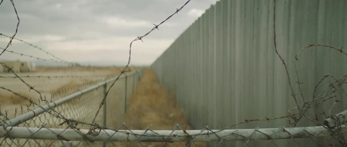 A mobile home sits in the desert behind the fence
