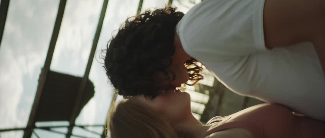 A man and woman kiss in an empty greenhouse on a windy day