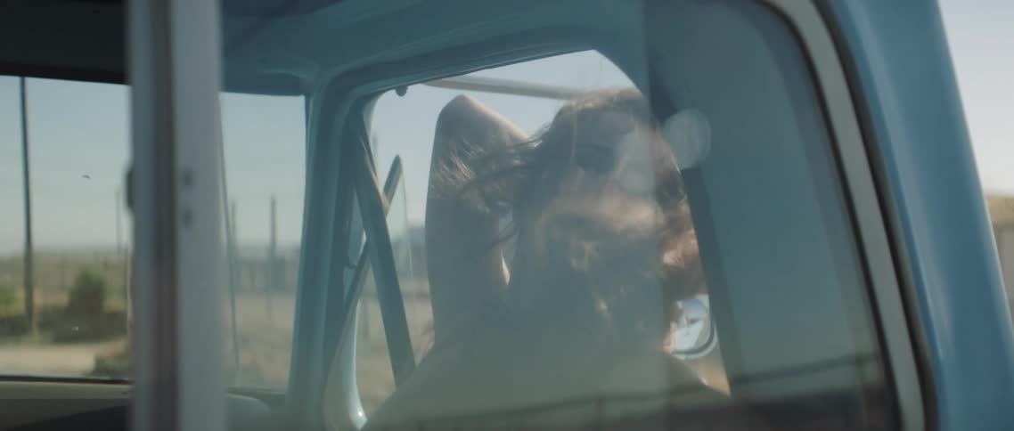 A woman in a vehicle with her head out the window with a landscape the sky and clouds in the background