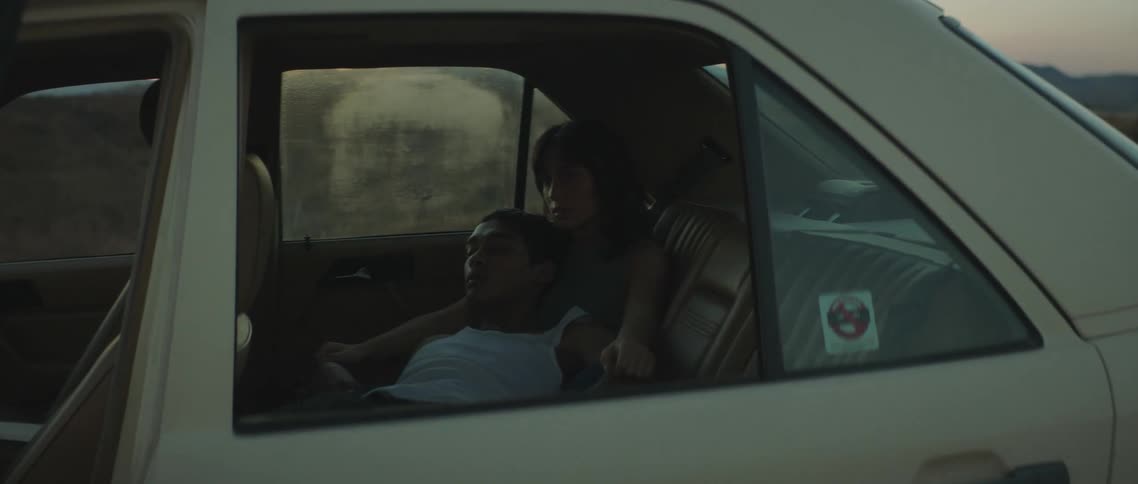 Young couple sitting on the back seat of a car parked on a rural area at sunset