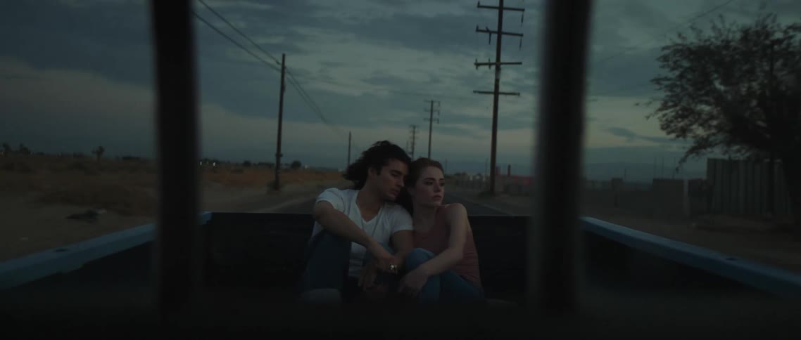 A man and a woman riding in the back of a pickup truck with the landscape the sky and clouds in the background