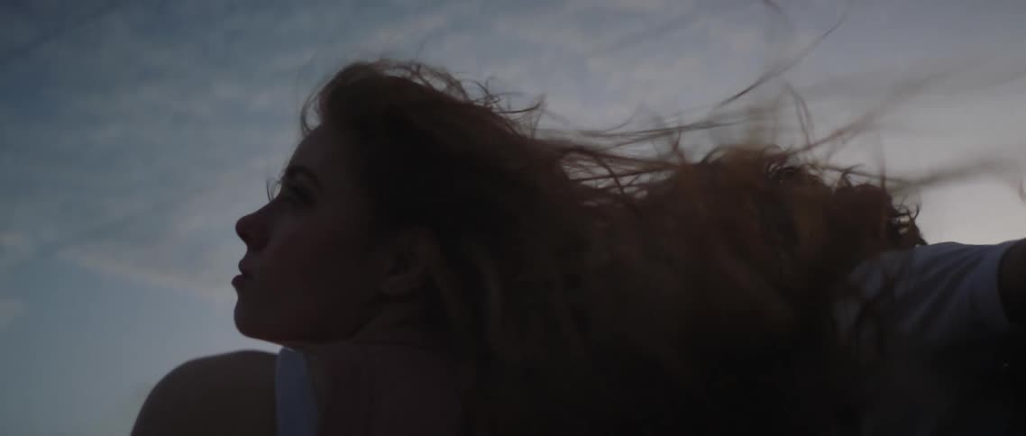 Young couple riding on the back of a truck with their hair blown by the wind at evening
