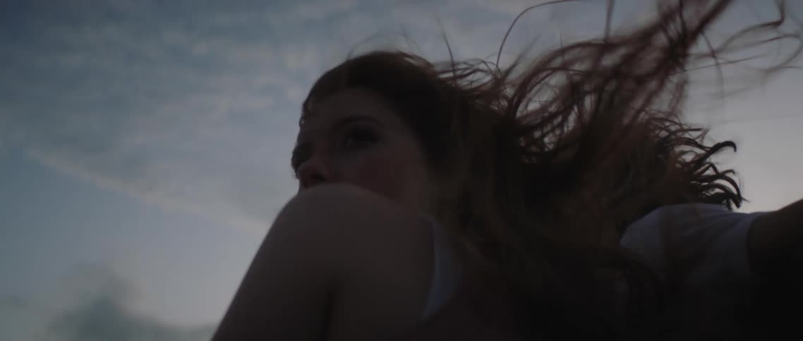 A womans hair blows in the wind under a partly cloudy sky with another person