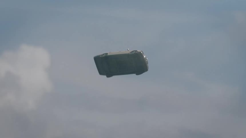 A vintage car spins through the air as it falls toward a field near a neighborhood