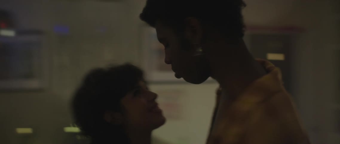 Man with orange shirt and woman hold each other and turn around while kissing each other in room with decorations