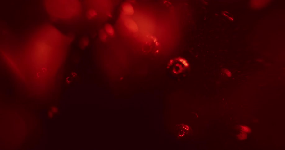 Bubbles move and shift as light glows through a deep red liquid