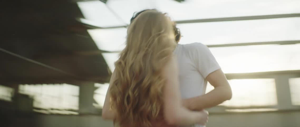Man with white shirt and jeans kisses woman wearing sleeveless shirt and jeans holding each other