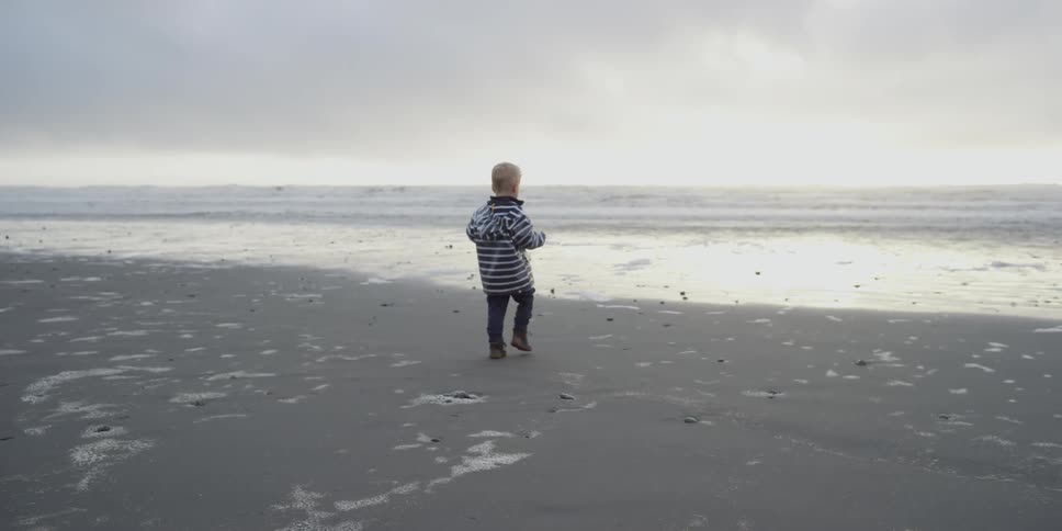 A boy in a blue jacket walks toward a beach