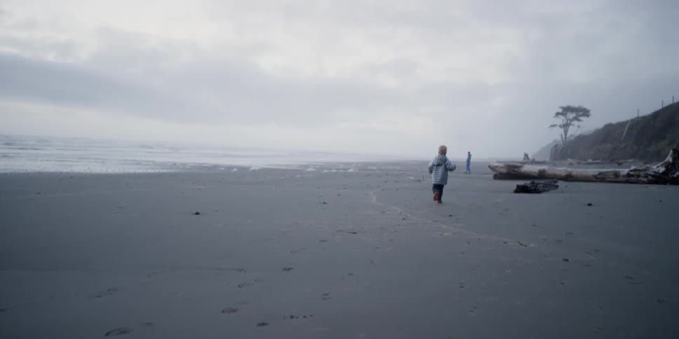 A young boy runs along a beach on a cloudy day