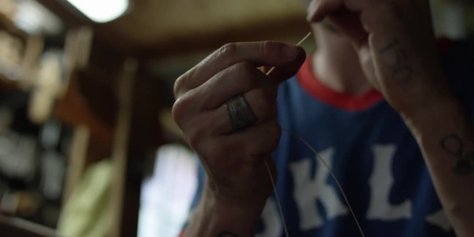A man pulls a string out and puts it in a needle
