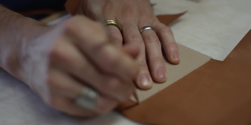 Someone tracing the outline of a stencil on a piece of leather