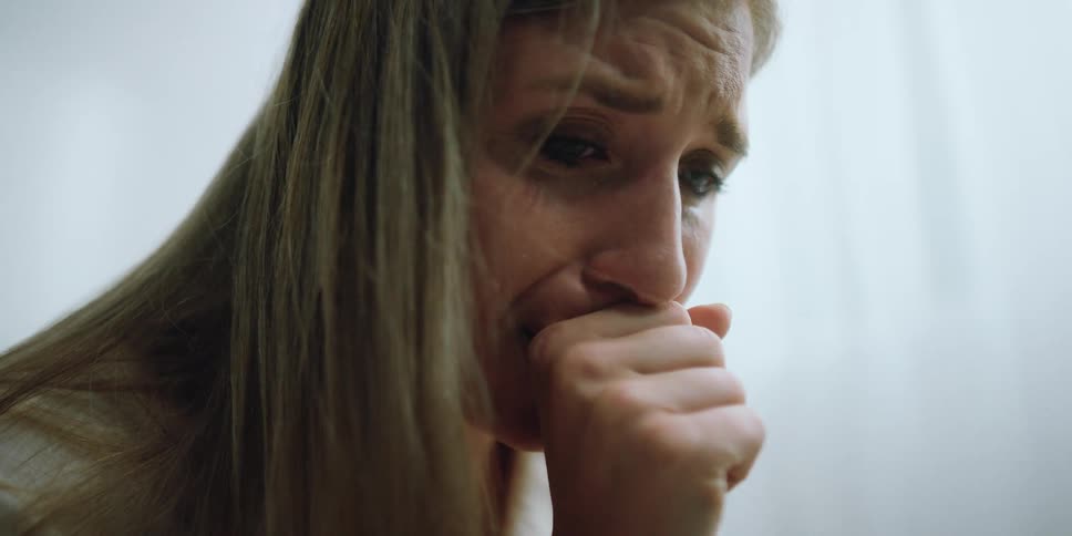 A woman is crying as she sits on the bed