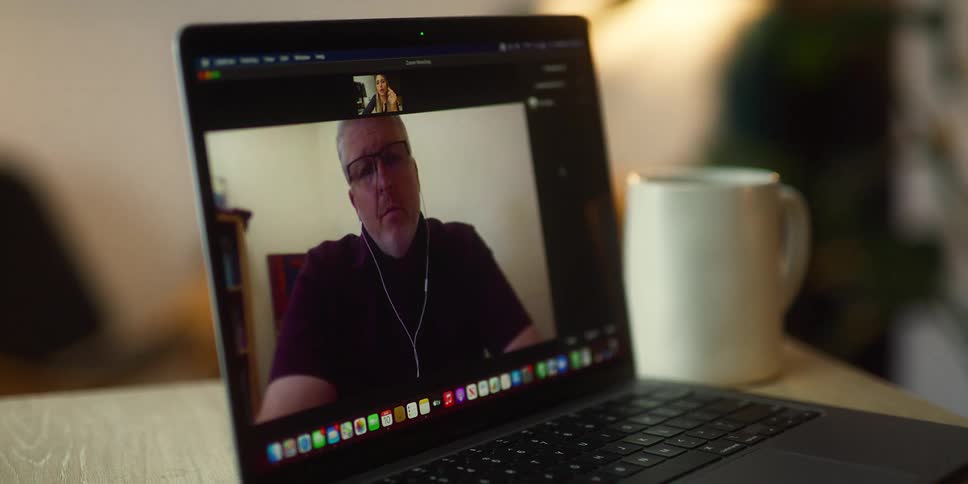 A woman in a room video chatting with a man on a laptop on a table with a wall in the background
