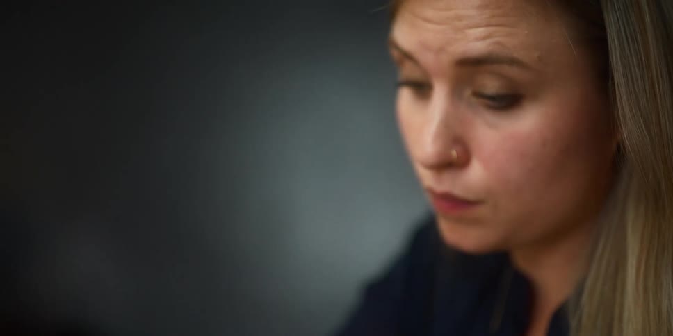 Blonde woman sitting at desk listens attentively and writes down on notebook