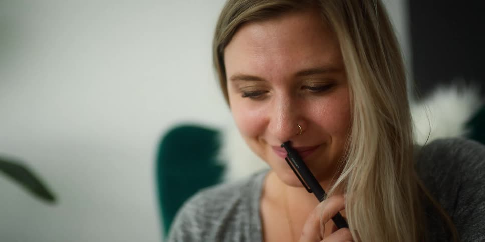 Blonde woman smiles while playing with a pen on the office