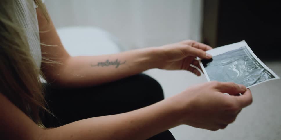 Blonde woman sitting down looks down at ultrasound baby picture