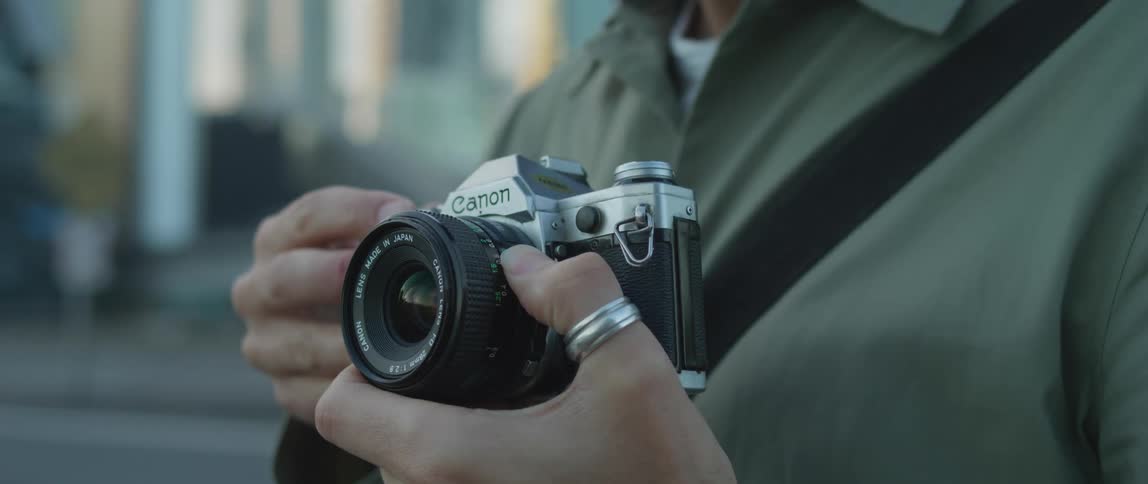 A man with a ring holding a camera with steps and a building in the background