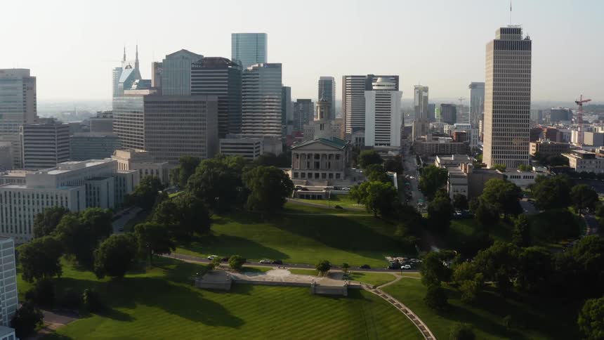 A park with green grass and trees surrounded by skyscrapers and a downtown city skyline