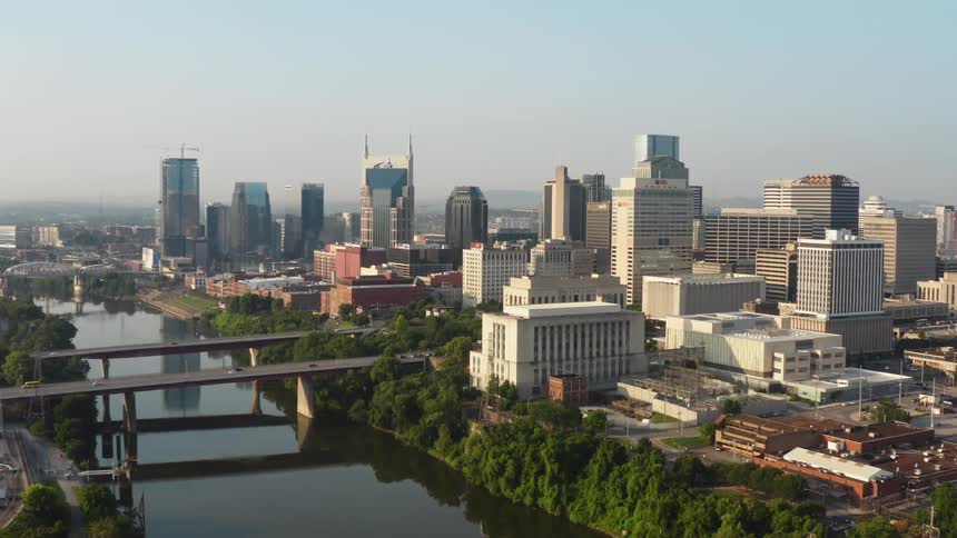 A city skyline with buildings and skyscrapers with a bridge and vehicles with the sky and clouds in the background