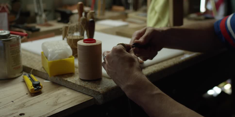 A man cuts some thread on a workbench
