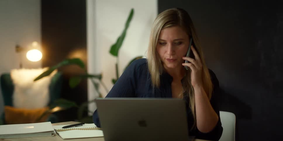 A woman is working at home using a smartphone and a laptop computer