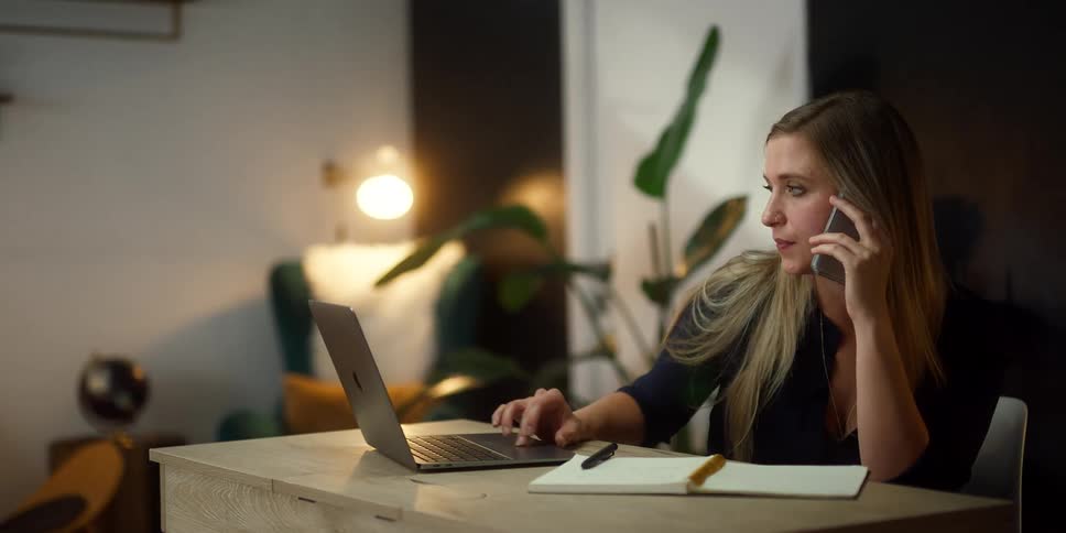A woman scrolling on a laptop while talking on a phone in an office setting