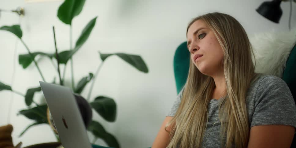 Blonde woman with grey shirt and nose ring sit at desk using grey laptop