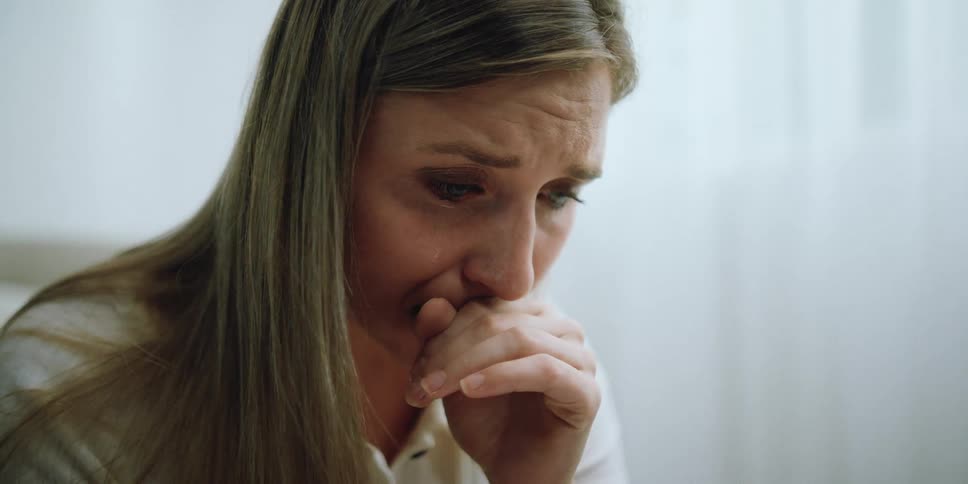 Woman with long hair cries with her hand up to her mouth