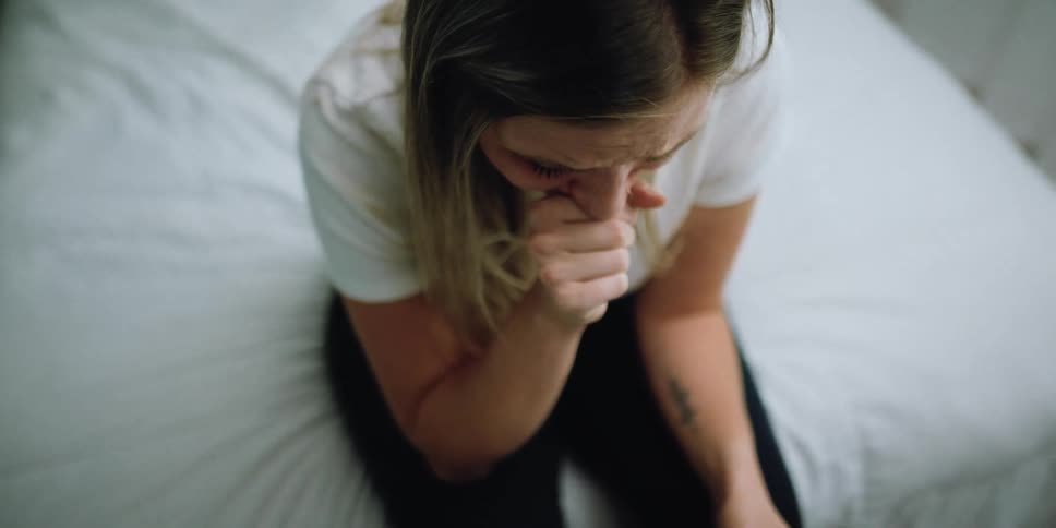 Blonde woman with white shirt and black pants looks down at ultrasound baby picture getting emotional