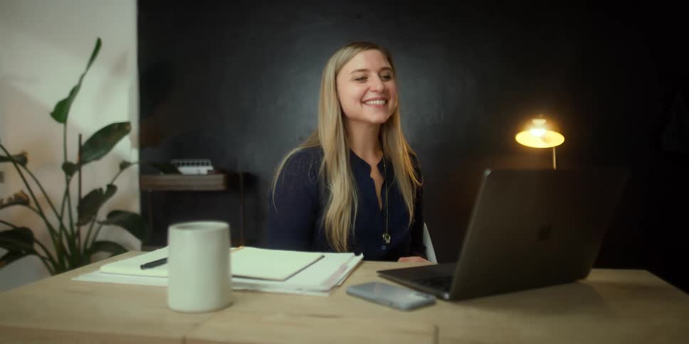 Young woman sitting at a desk in the office smile while greeting someone on a video call