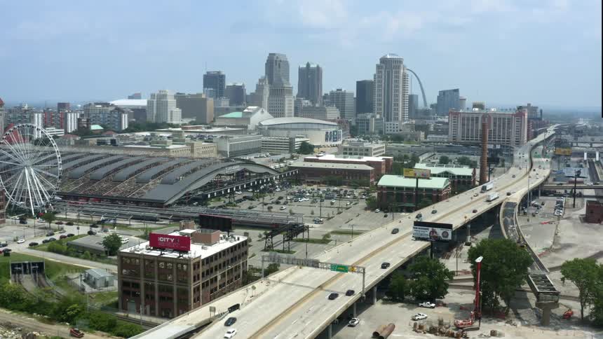 A city skyline with buildings and skyscrapers a highway and a ferris wheel with the sky and clouds in the background