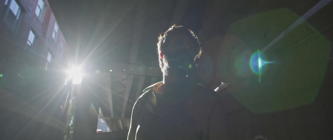 Sunlight over a young bearded man standing under a bridge in the city