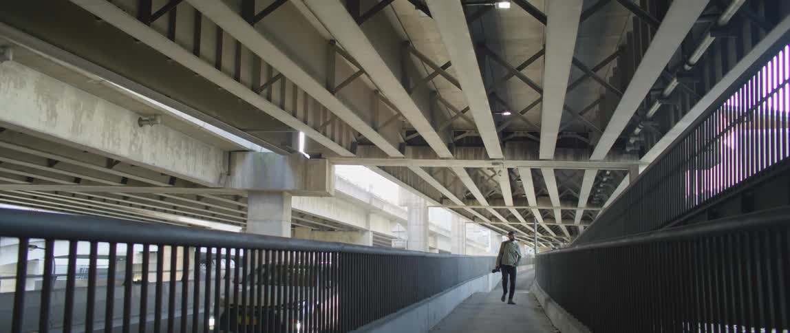 Young man walking next to the highway under a bridge
