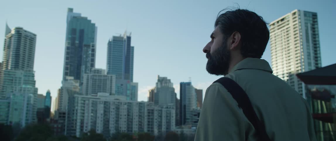 Man stands overlooking treed area in middle of city under blue sky