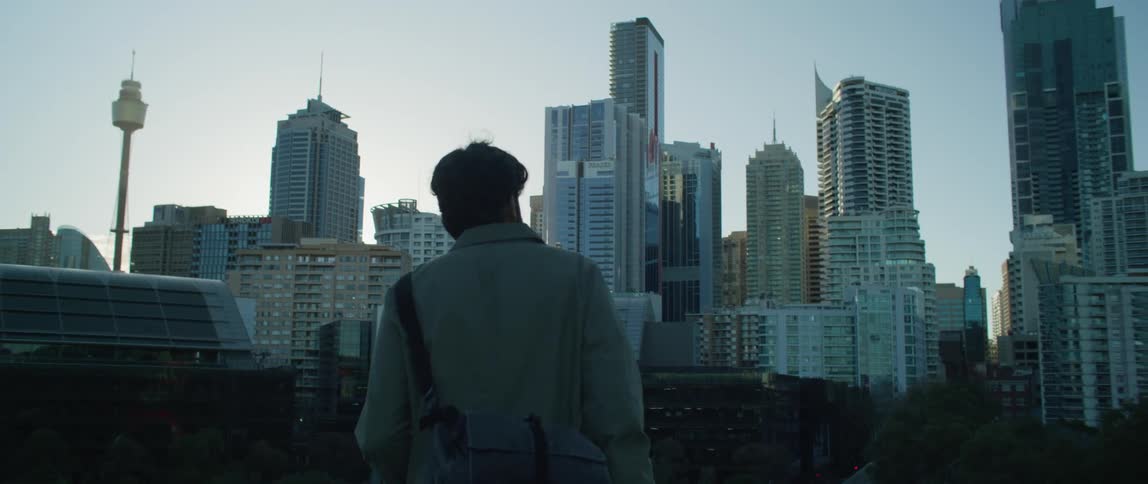 A man approaches the edge of a balcony and looks out at the skyscrapers in the distance