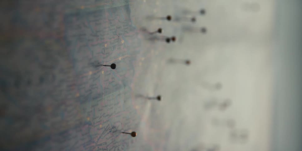 Hand placing a pin over a map hanging on the wall inside a dimly lit room
