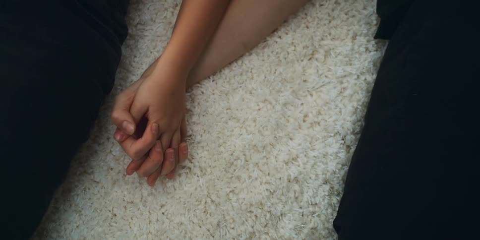 Two people lying on a white rug holding hands