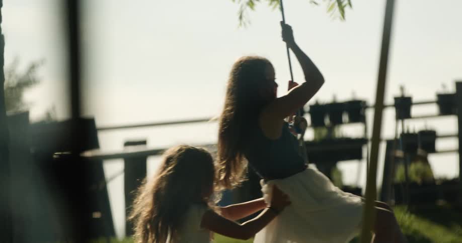 A young girl pushes her sister on a tire swing in their yard
