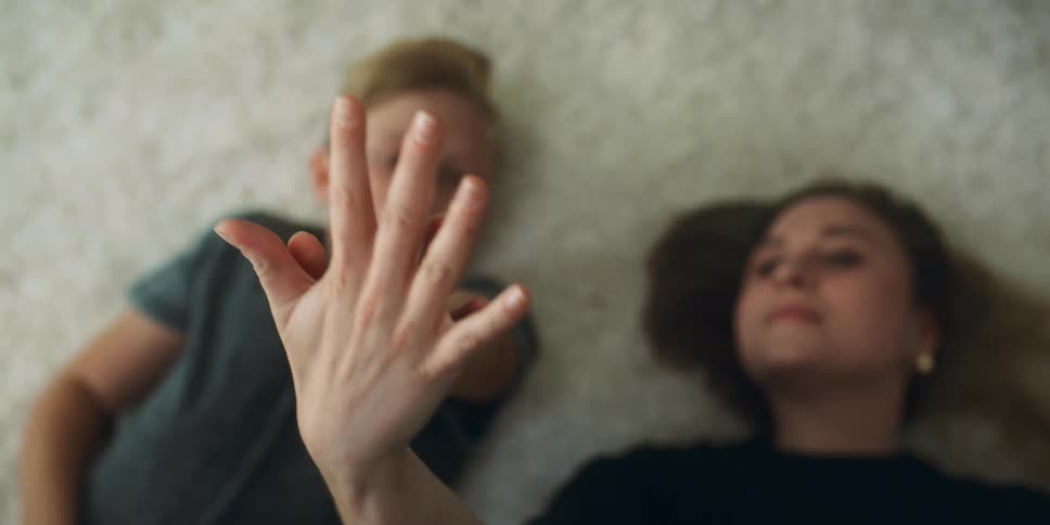 Mother and son lie on their back on carpet their hands touching in the air
