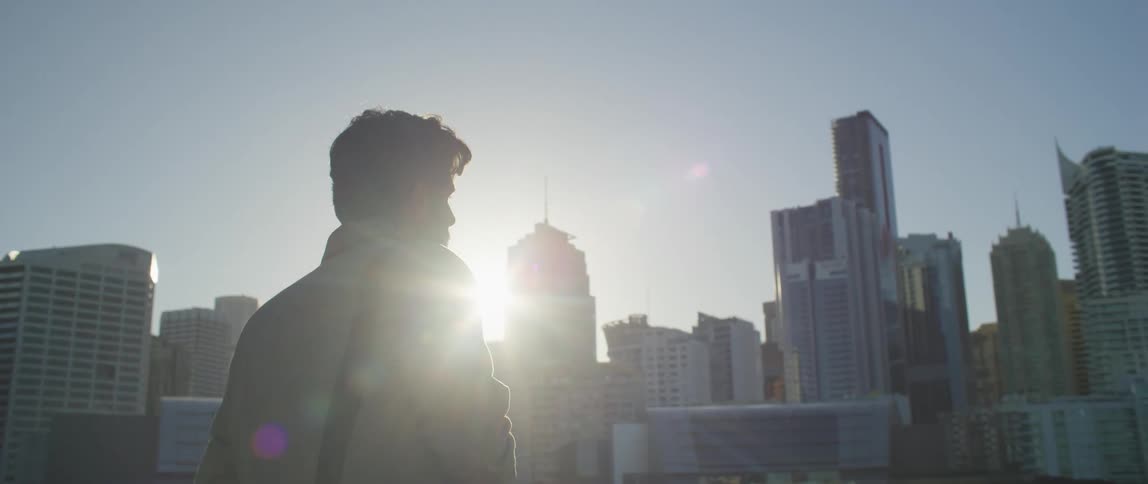 Male photographer with beard jacket and bag takes photographs of city buildings at sunset