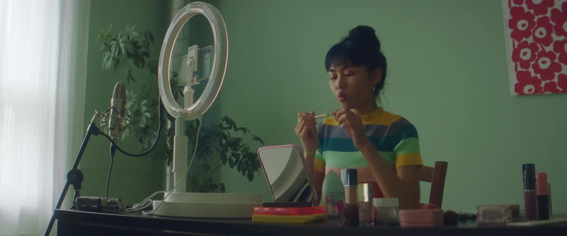 Woman with colorful shirt demonstrates how putting on makeup on filming herself on smartphone