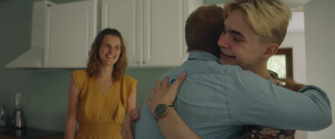 A boy is greeted by a couple in the kitchen