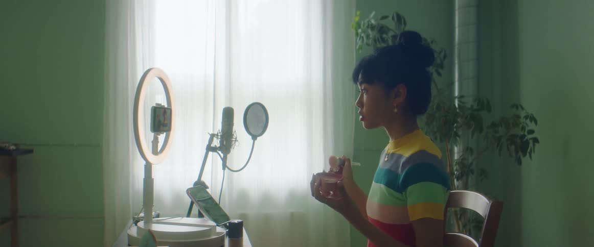 A woman films a makeup tutorial inside a room with special lighting and microphones
