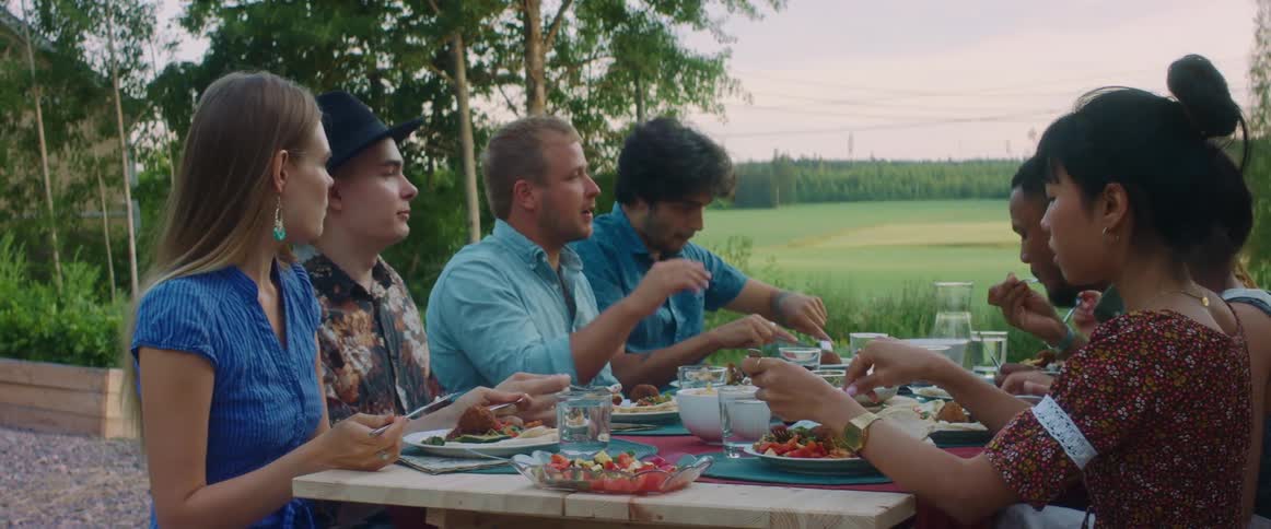 Group of men and women sit at a picnic table and talk and eat