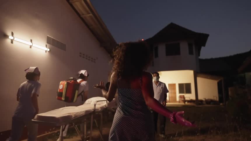 Woman runs towards a doctor that is standing next to an ambulance stretcher while two nurses walk by